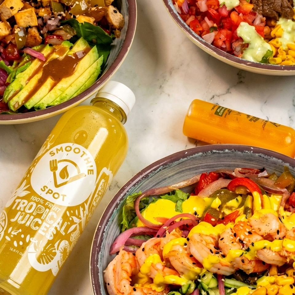 Three colorful salad bowls with various toppings and two bottles of Smoothie Spot Tropical Juices.
