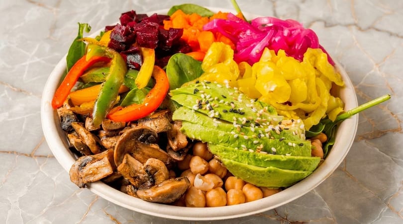 Colorful vegan bowl with avocado, chickpeas, mushrooms, bell peppers, beets, and pickled onions.