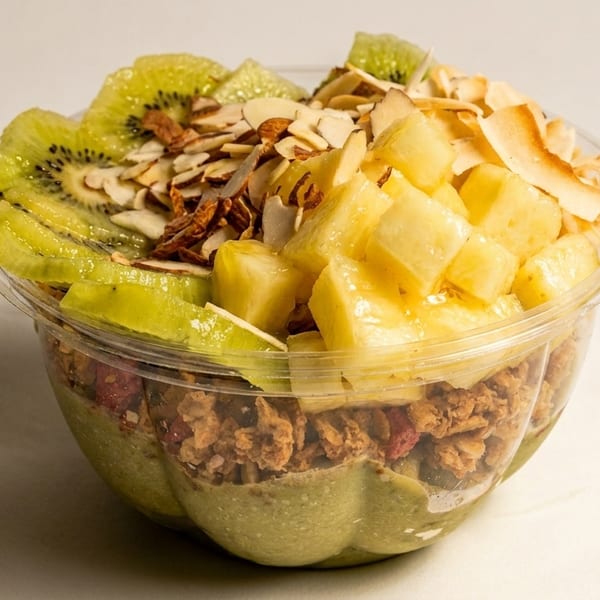 A vibrant smoothie bowl with kiwi, pineapple, almonds, and granola in a clear cup.
