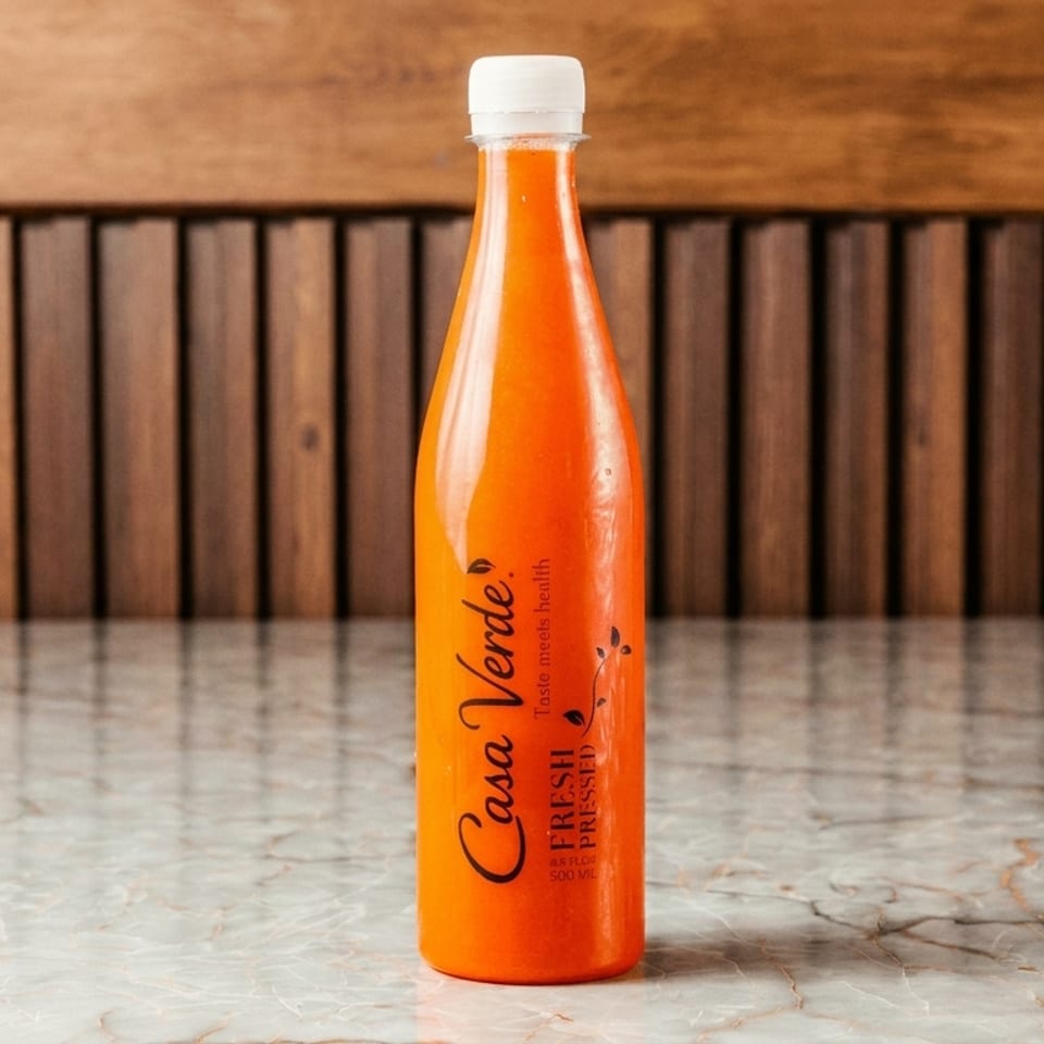 A Casa Verde fresh pressed juice bottle sits on a marble table against a wooden slatted wall.