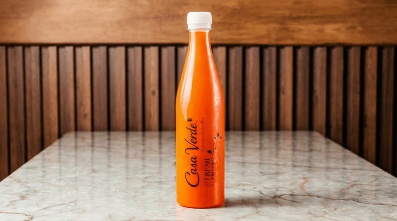 A Casa Verde fresh pressed juice bottle sits on a marble table against a wooden slatted wall.