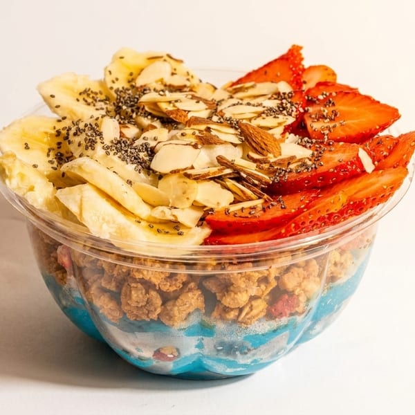 A vibrant blue smoothie bowl topped with bananas, strawberries, granola, almonds, and chia seeds.