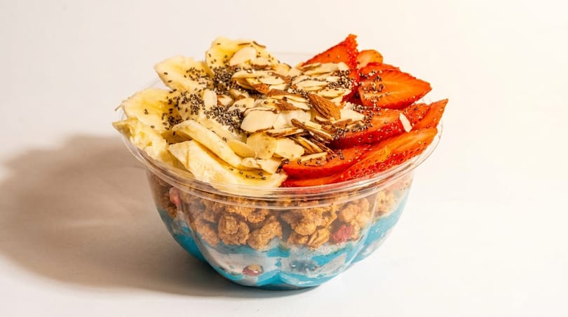A vibrant blue smoothie bowl topped with bananas, strawberries, granola, almonds, and chia seeds.