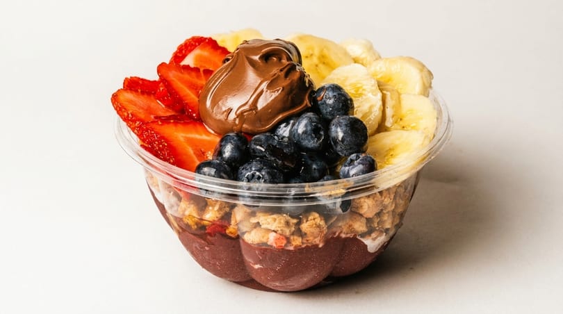 A vibrant acai bowl with strawberries, blueberries, bananas, granola, and a dollop of chocolate spread.