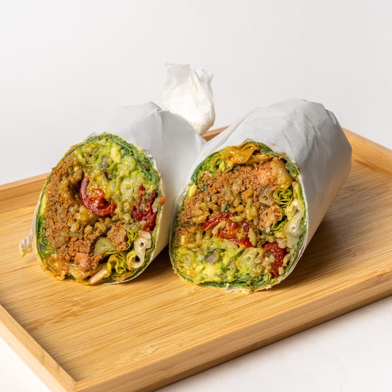 Two halves of a healthy Casa Verde burrito, filled with meat, rice, avocado, and vegetables.