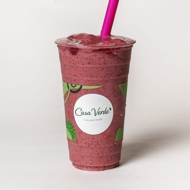 Casa Verde berry smoothie in a branded cup with a pink straw against a white background.